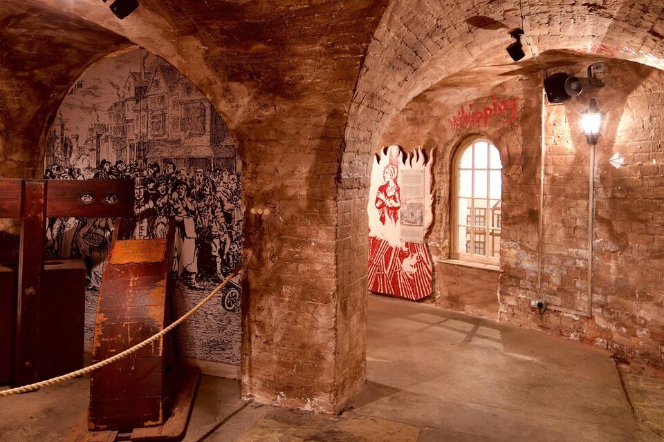 An underground passage with arched brick ceilings, historical murals, and a rope barrier.