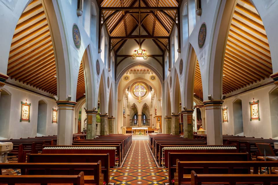 Ein Kircheninneres mit Holzbänken, einem zentralen Altar und einer gewölbten Decke.