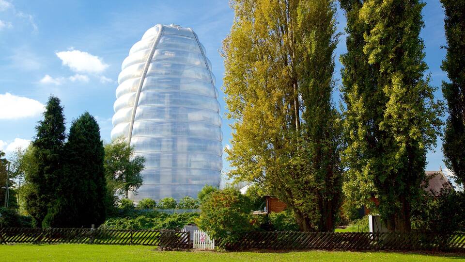 A large, transparent building with a unique, layered design, surrounded by lush green trees and a well-maintained park.