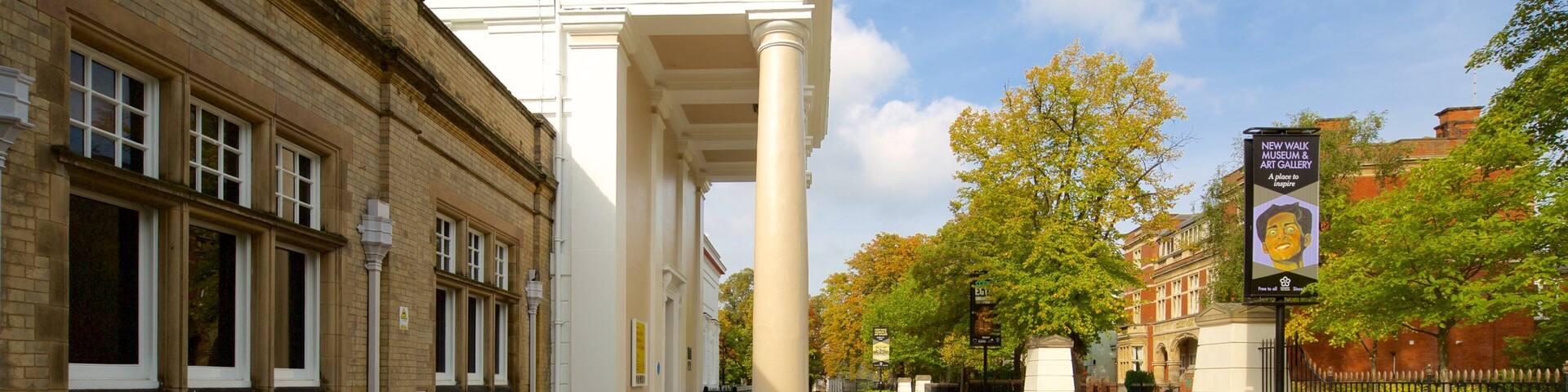 A street with classical architecture, including a building with columns and a sign for the New Walk Museum & Art Gallery.
