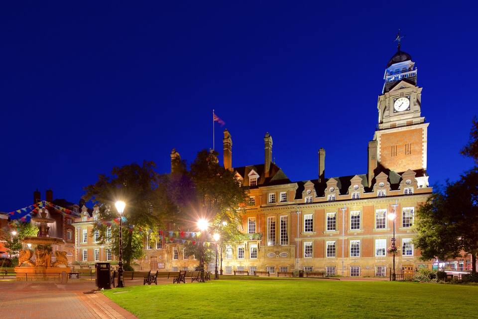 A historic building with a clock tower, surrounded by a well-maintained lawn and street lamps.
