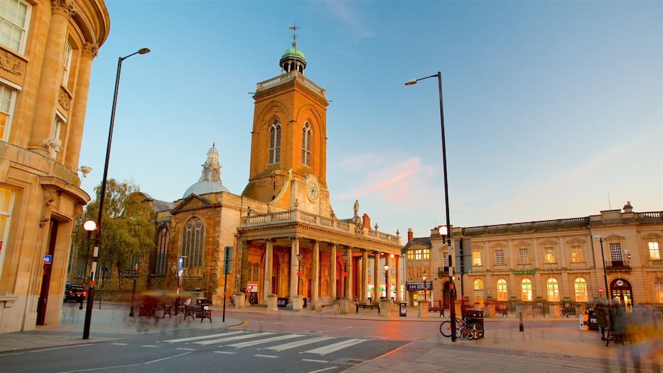 A historic building with a clock tower, a street with benches, and a clear sky.