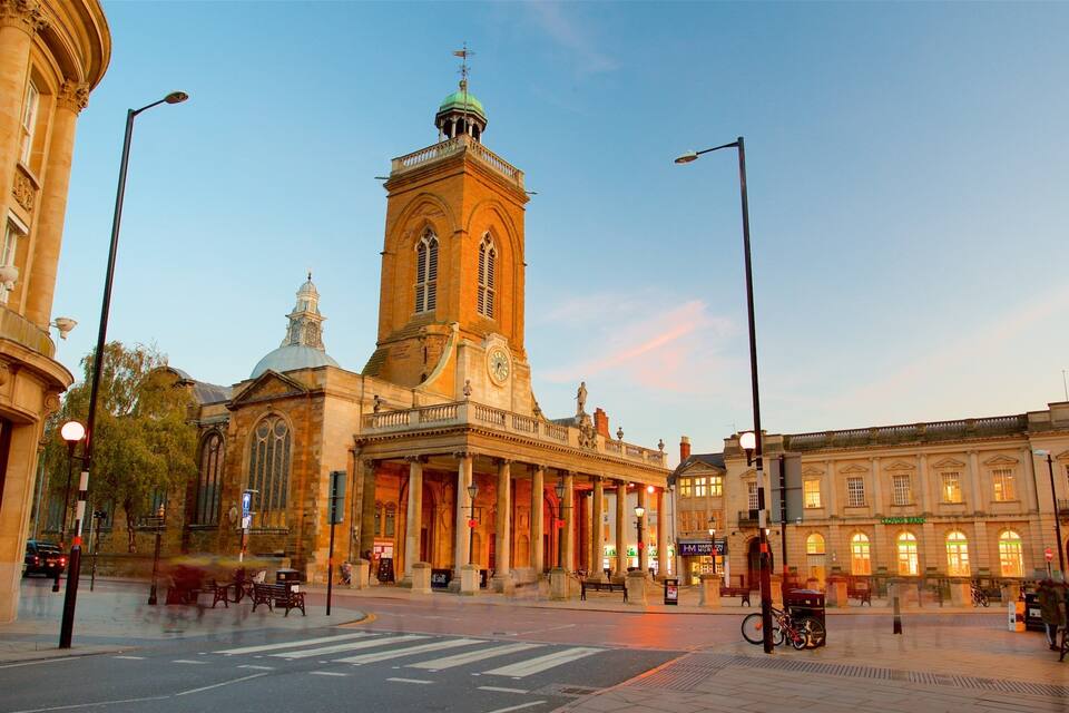 A historic building with a clock tower, a street with benches, and a clear sky.
