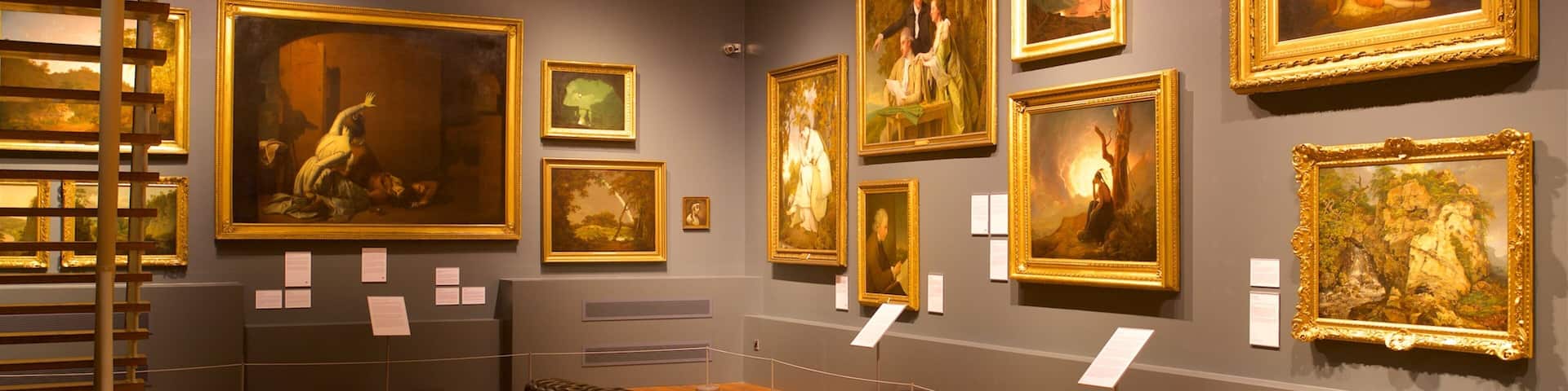 A gallery with classical paintings on the walls and wooden benches in the center.