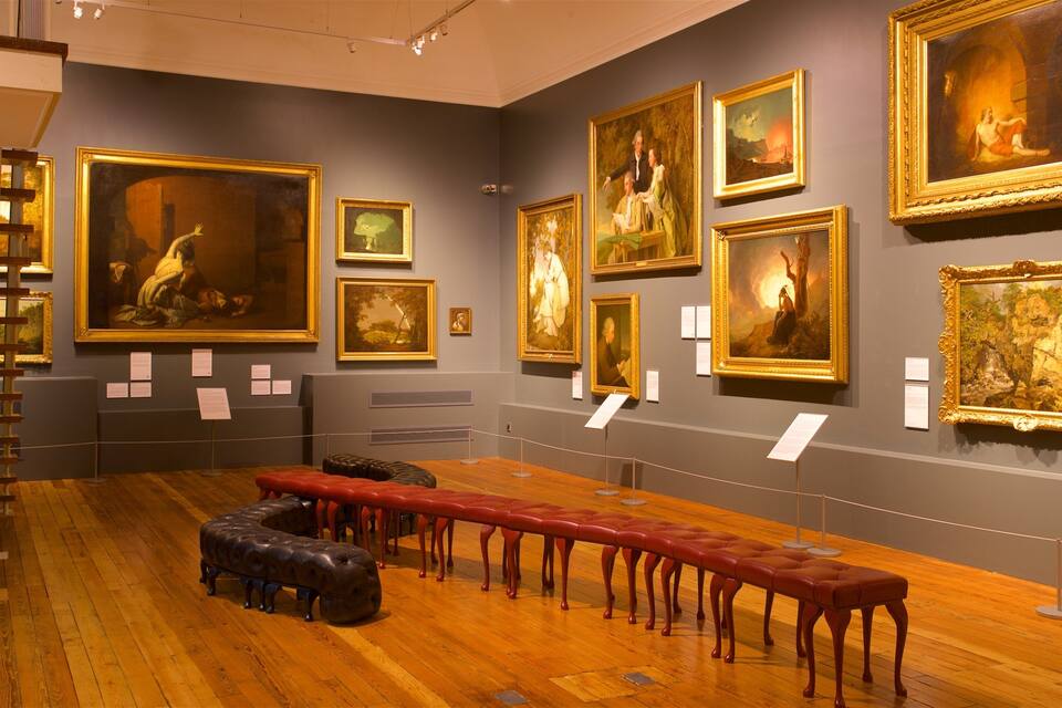 A gallery with classical paintings on the walls and wooden benches in the center.