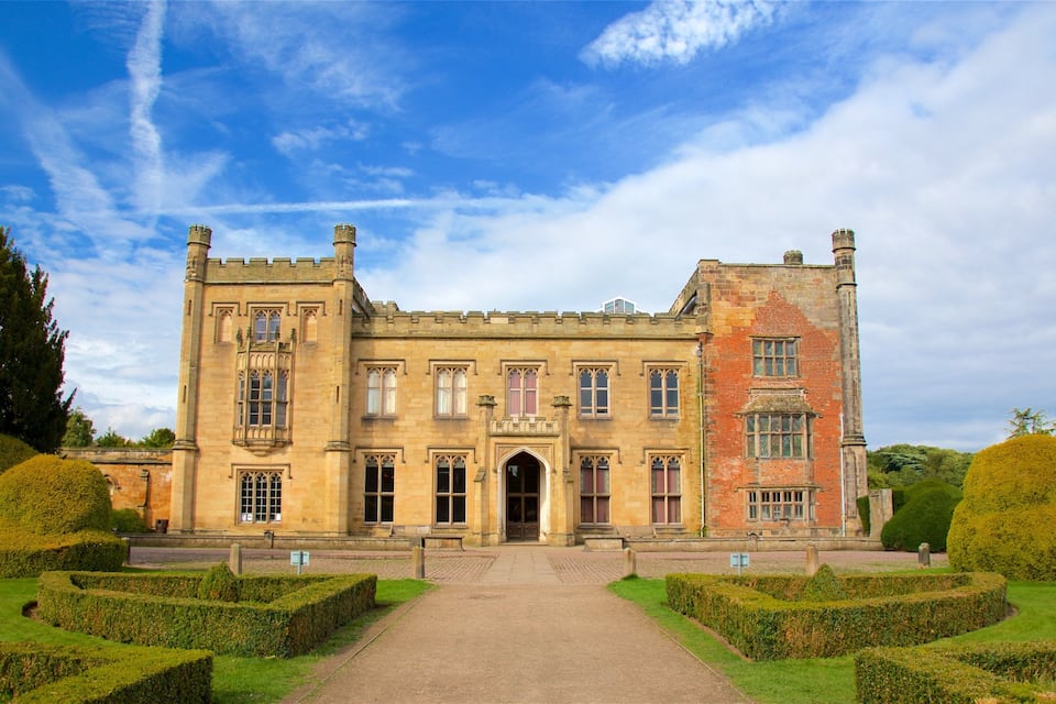 A large, historic building with a symmetrical facade, a central entrance, and a well-manicured garden with hedges and trees.