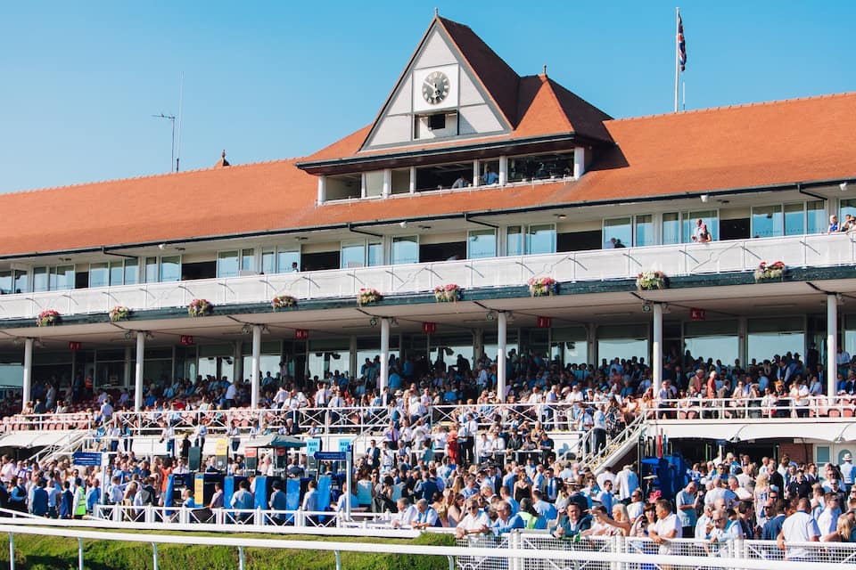 A large stadium with a clock tower, covered seating, and a crowd of spectators.