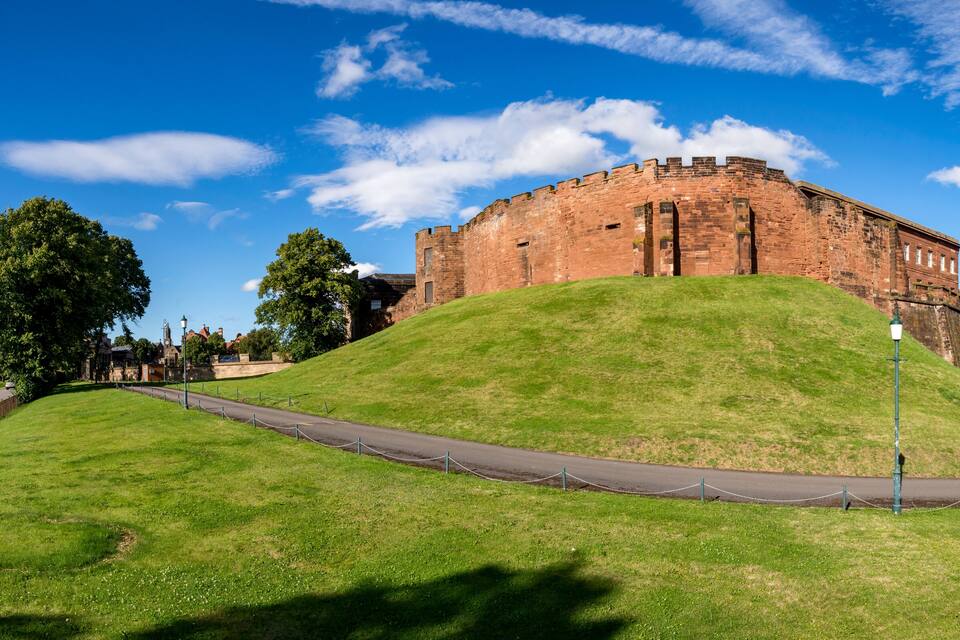 A large brick castle on a grassy hill under a clear blue sky.