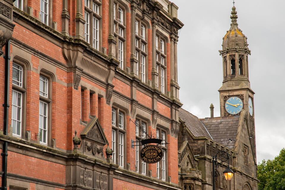 A historic building with a clock tower and a sign reading "Grosvenor 1886 Museum".