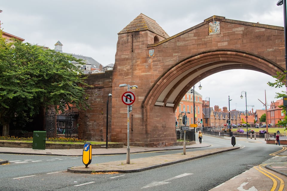 A historic stone arch bridge with a crest, a no left turn sign, and a one way sign on a city street.