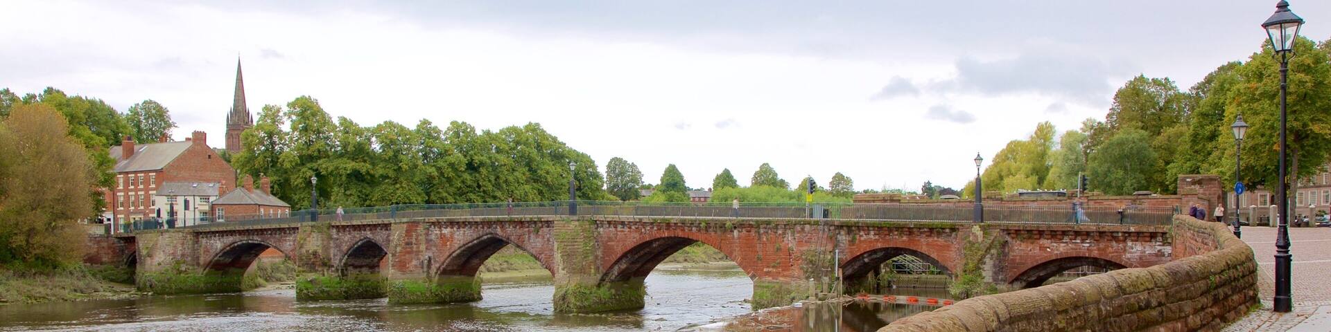 A stone bridge over a river with a stone wall on the right and a church in the background.