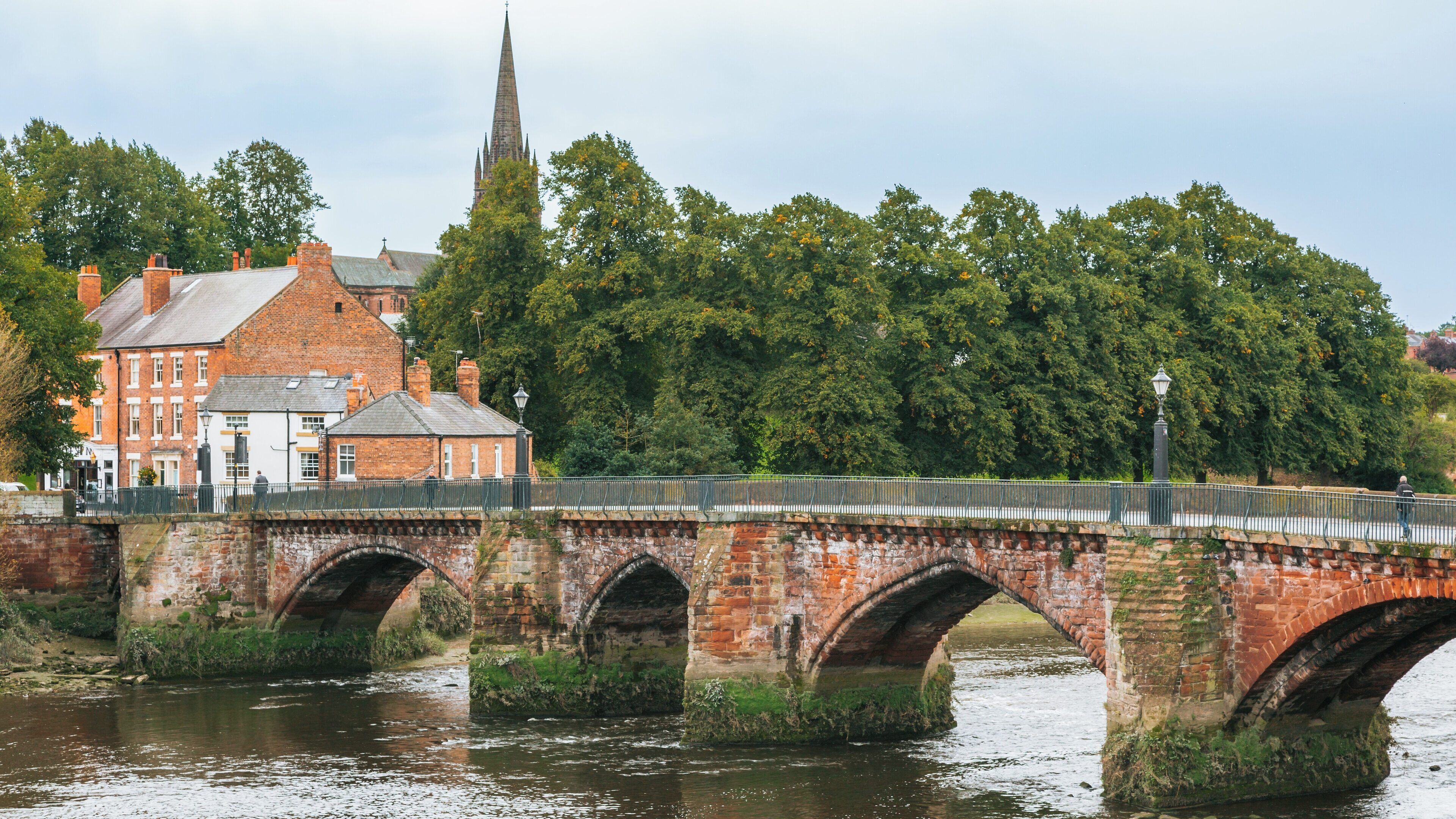 Historic Old Dee Bridge spanning the River Dee in Chester, England, surrounded by lush greenery and charming architecture