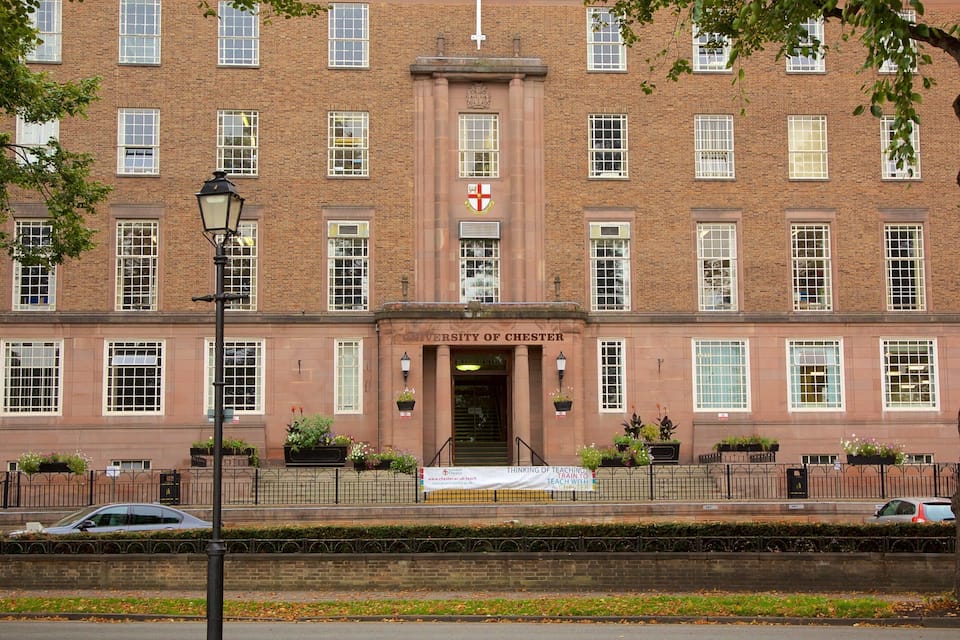 The University of Chester building with a red brick facade, large windows, and a banner at the entrance.