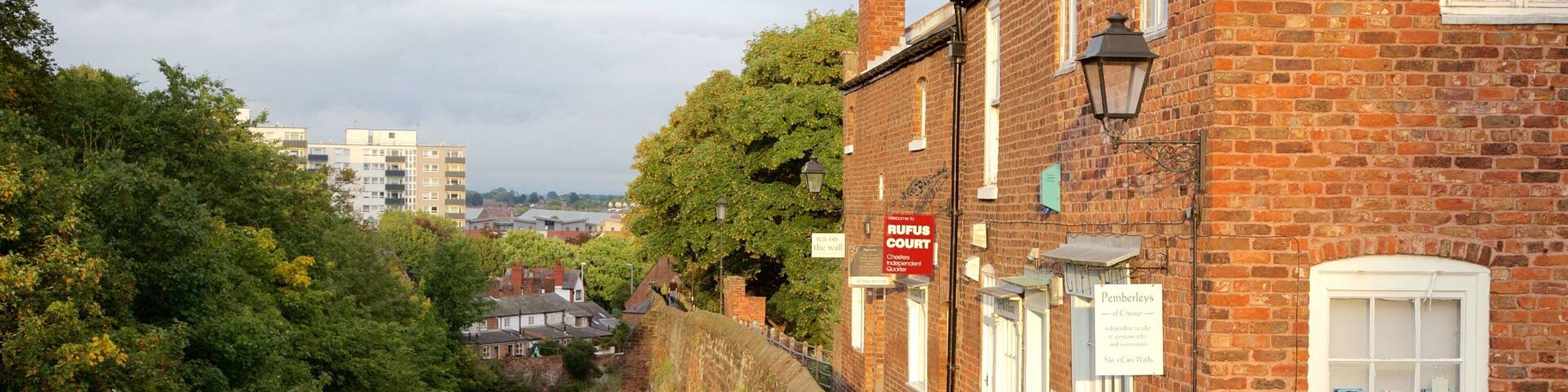 A riverside walkway with brick buildings, a sign for RUFUS COURT, and a sign for Pemberleys.