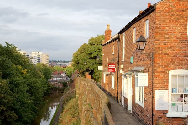 A riverside walkway with brick buildings, a sign for RUFUS COURT, and a sign for Pemberleys.