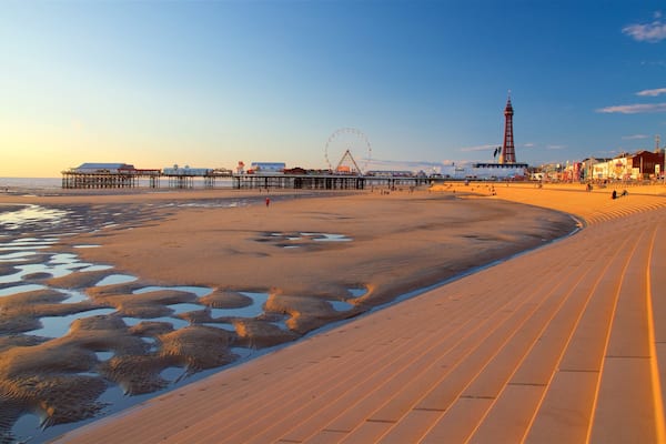 A beach with a boardwalk, a pier, a Ferris wheel, and a lighthouse.