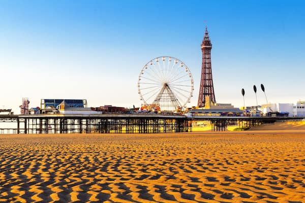 Ein Strand mit einem Riesenrad, einem hohen Turm und einer Seebrücke.