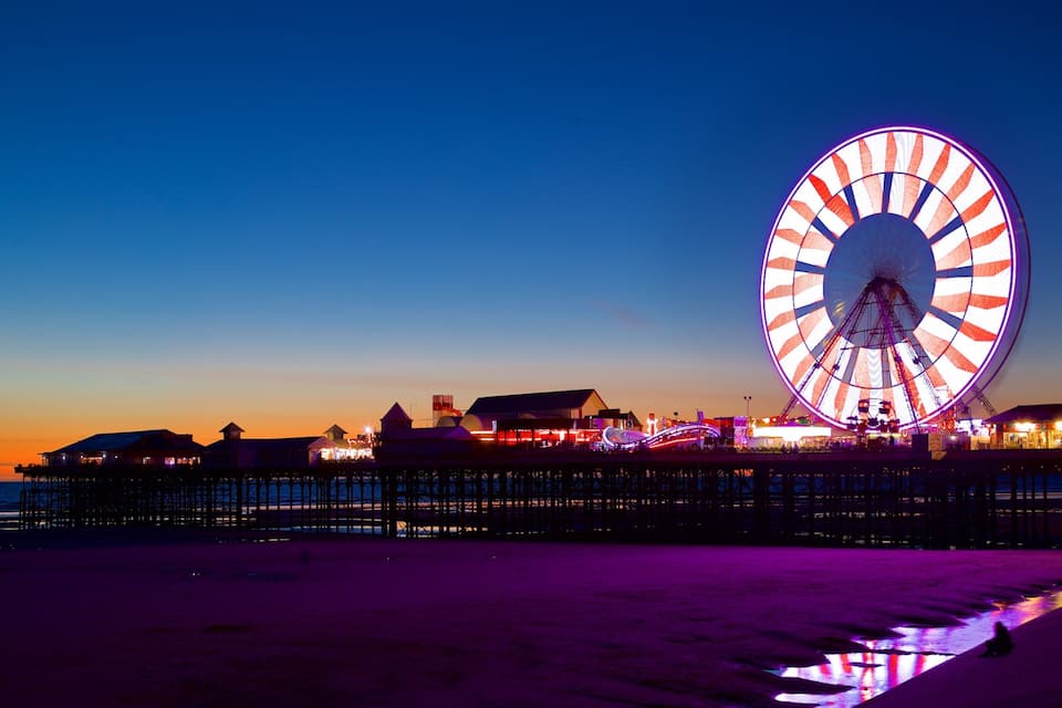 A beach with a large illuminated Ferris wheel at sunset.