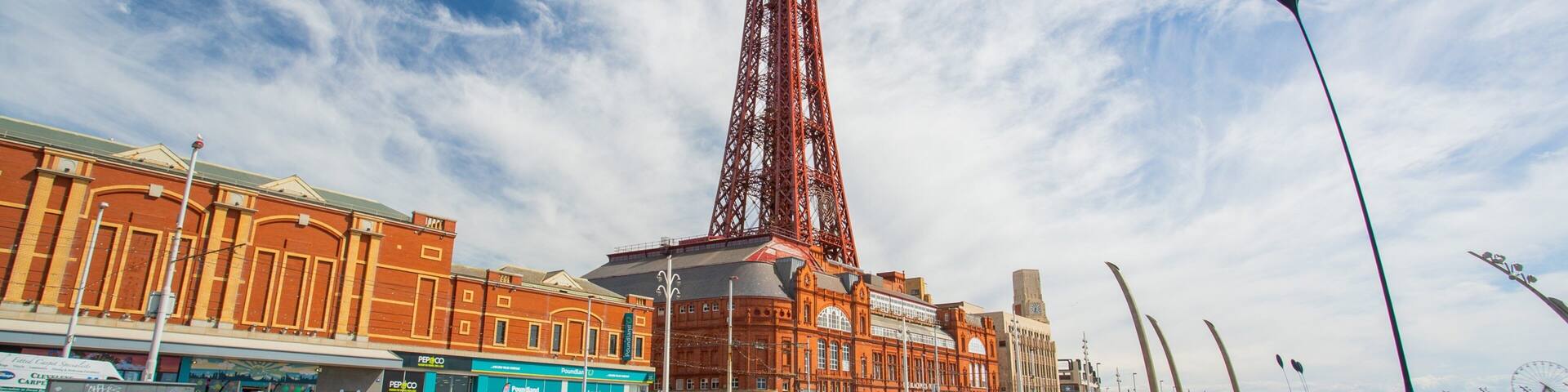 A large red tower, a plaza with people, and buildings with shops.