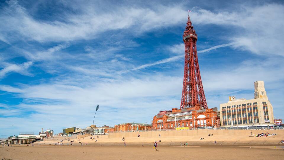 A beach with a tall red tower and a large building with a clock tower.