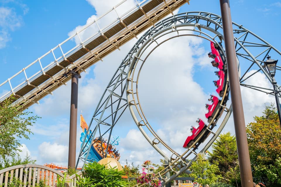 A roller coaster with red cars, a bridge, and a pirate-themed attraction.