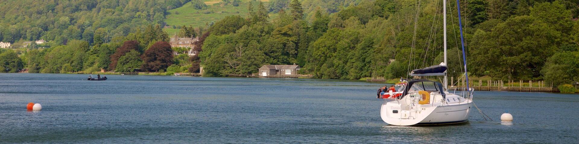 Un voilier sur un lac paisible, avec en arrière-plan des collines verdoyantes et un ciel dégagé.