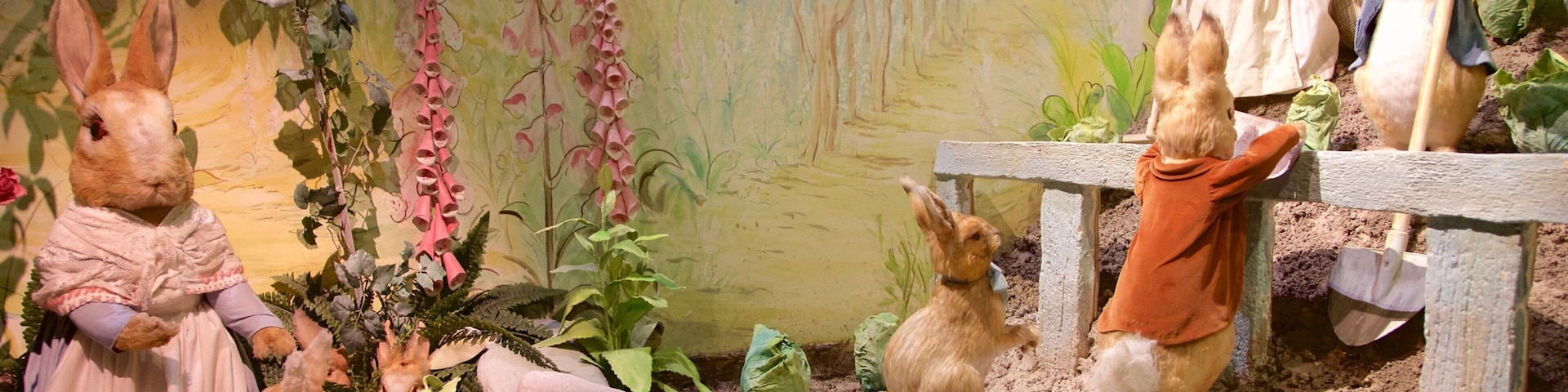 Cena de jardim com figuras de coelhos vestidos, cercados por plantas e pedras.