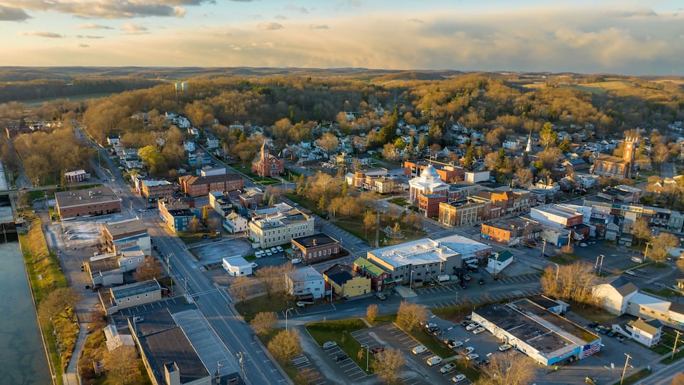An aerial view of a town with a river on one side, a mix of commercial and residential buildings, and a prominent church with a steeple.