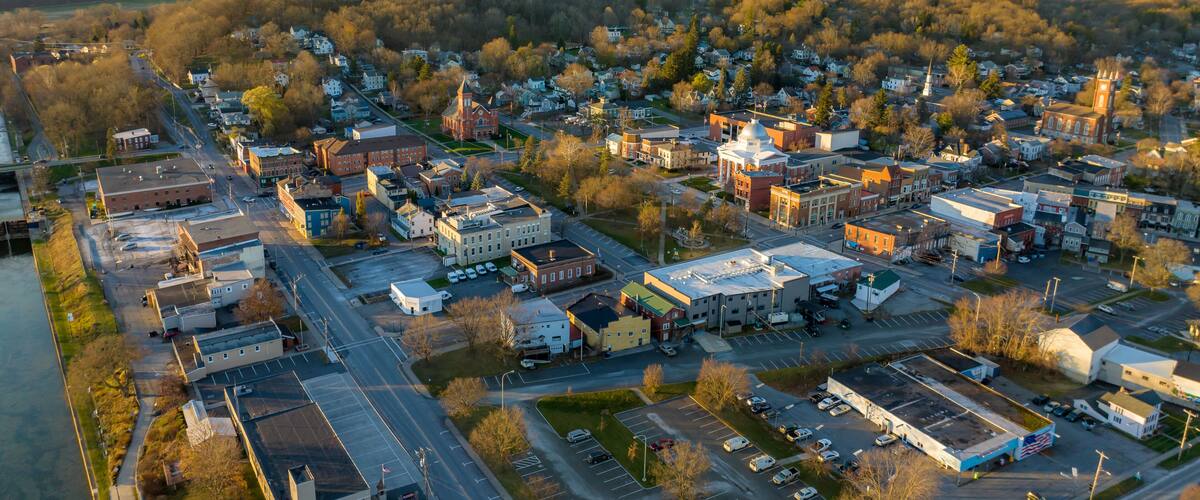 An aerial view of a town with a river on one side, a mix of commercial and residential buildings, and a prominent church with a steeple.