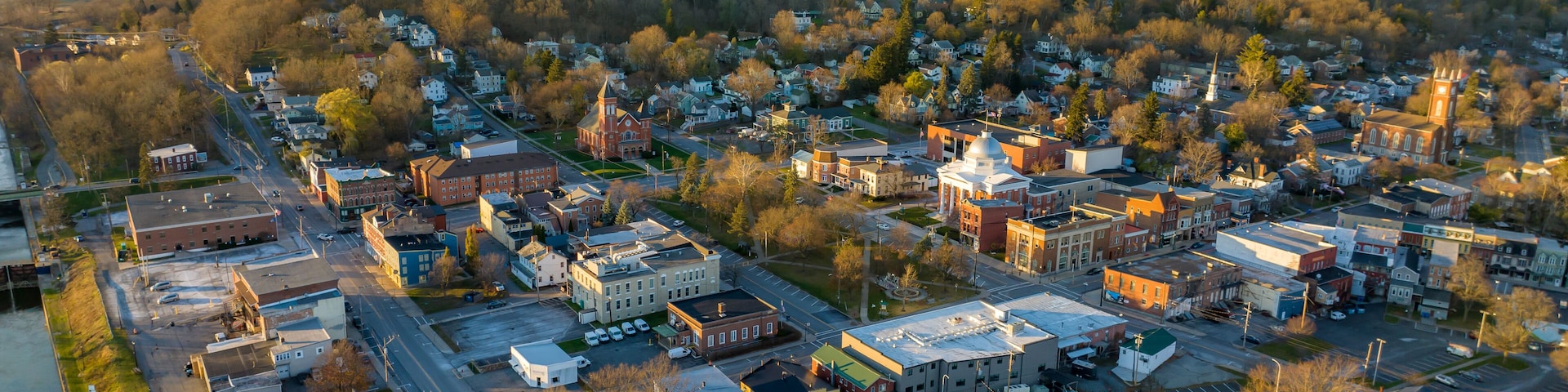 An aerial view of a town with a river on one side, a mix of commercial and residential buildings, and a prominent church with a steeple.