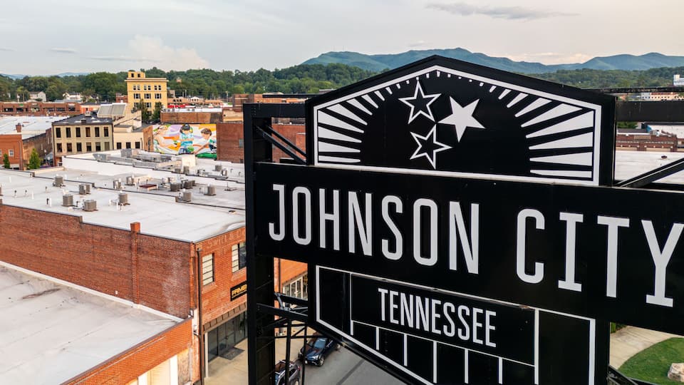 A sign for Johnson City, Tennessee, with a view of the cityscape and mountains in the background.
