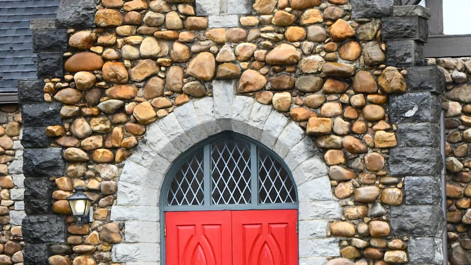 A stone building with a red door and a cross on the roof.