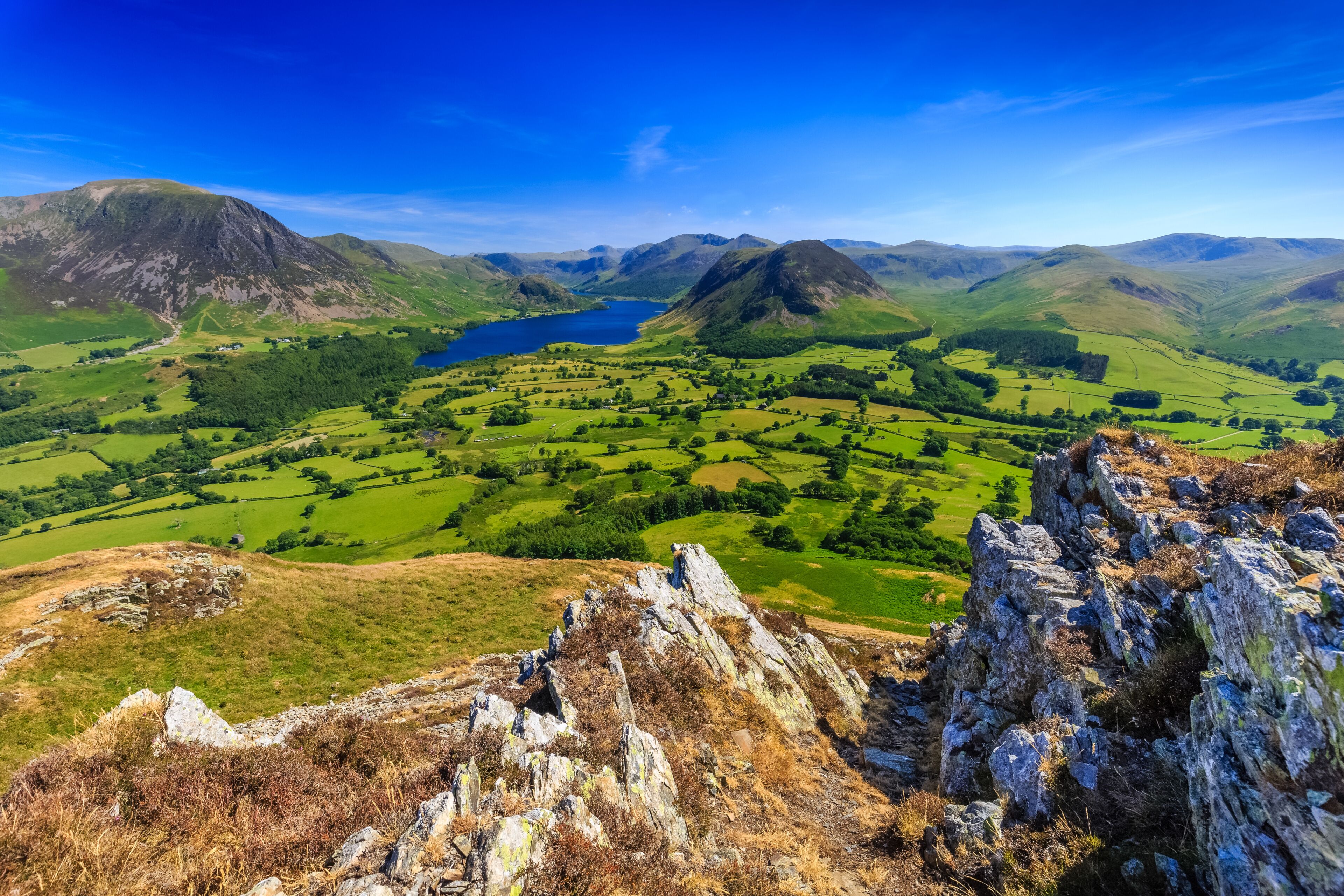 A mountainous landscape with a lake, green fields, and rocky outcrops.