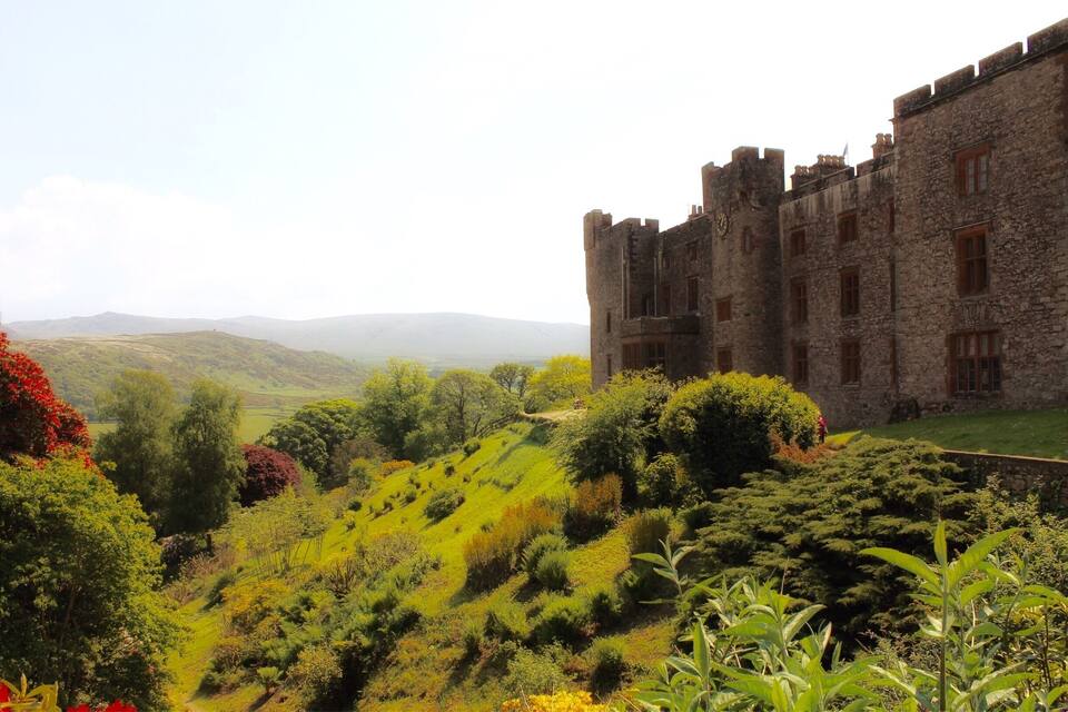 Un château entouré d’une végétation luxuriante et de collines ondoyantes.