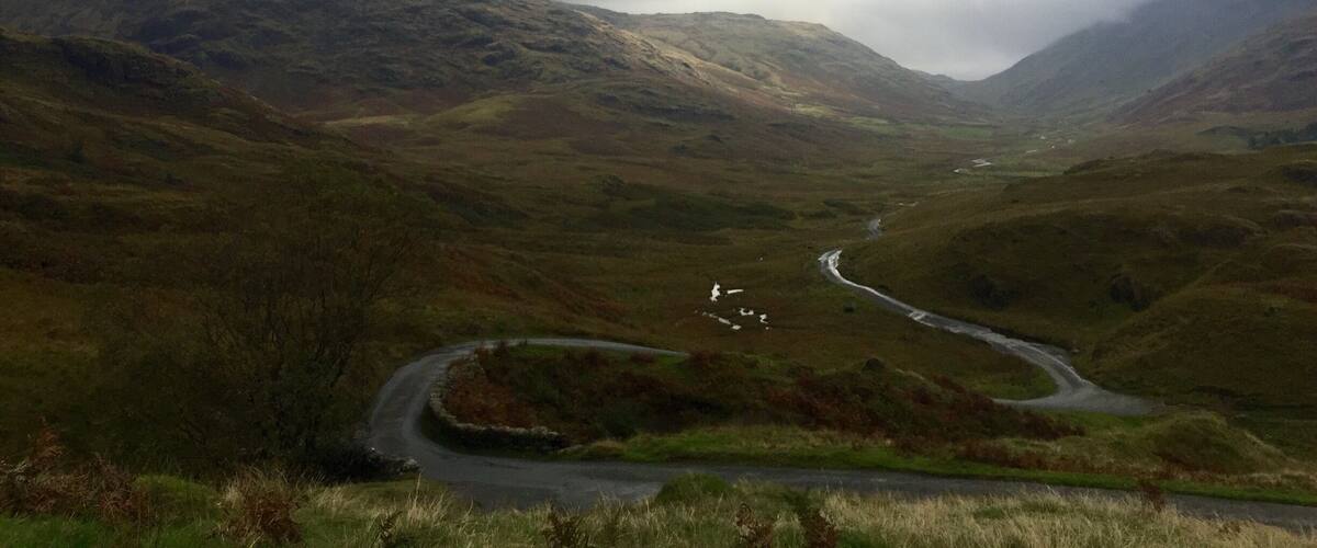 A winding road through a mountainous landscape with a cloudy sky.