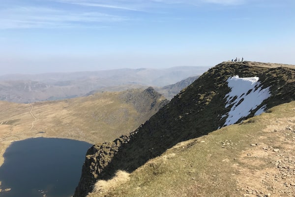A mountainous landscape with a clear sky, a lake, and a group of people on a ridge.