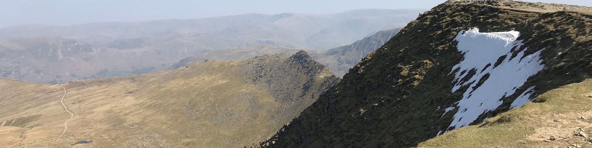 A mountainous landscape with a clear sky, a lake, and a group of people on a ridge.