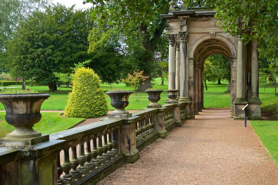 A formal garden with a gravel pathway, ornate columns, and classical architecture.