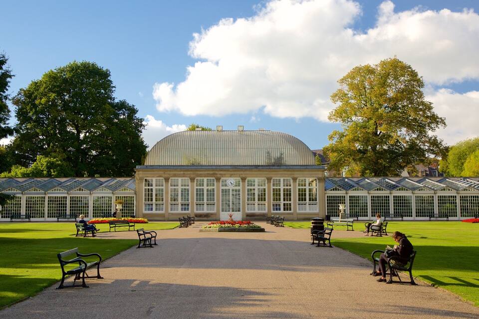 A large glass conservatory with a dome roof, surrounded by a well-manicured lawn and benches.