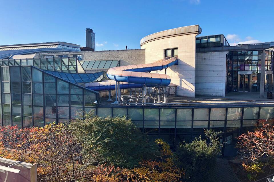 A modern building with a glass facade, a curved structure, and a water slide.