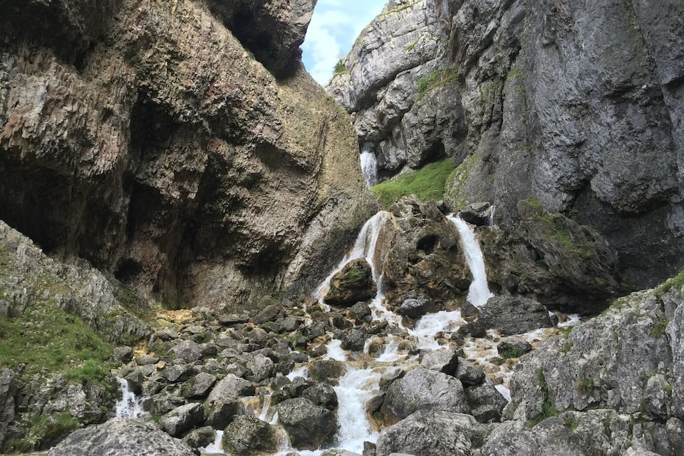 Un congost amb una cascada rocosa, penya-segades escarpades i vegetació escassa.