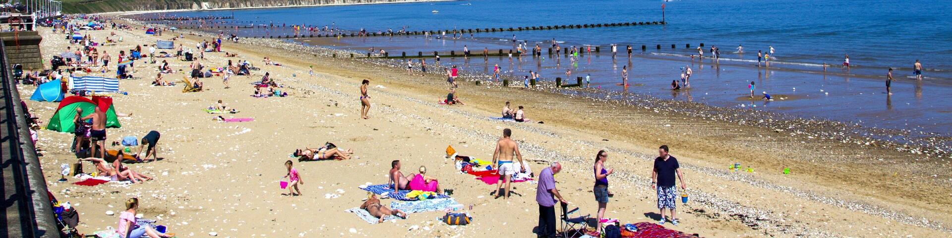 A crowded beach with people sunbathing and swimming.