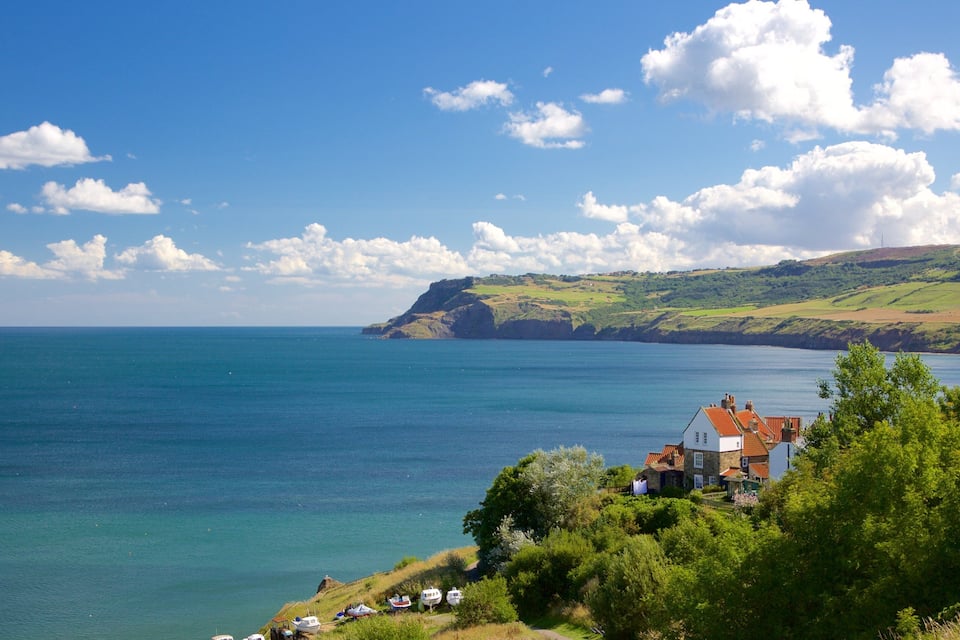 A coastal landscape with a clear sky, a calm sea, and a small village with houses and boats.