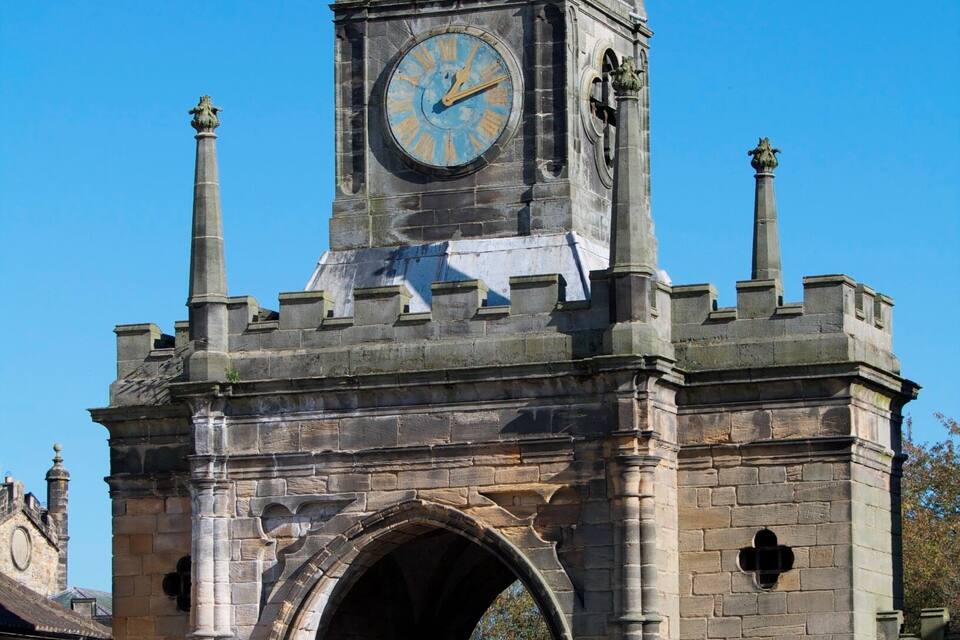 A historic stone clock tower with a weather vane, an archway, and a clear blue sky.