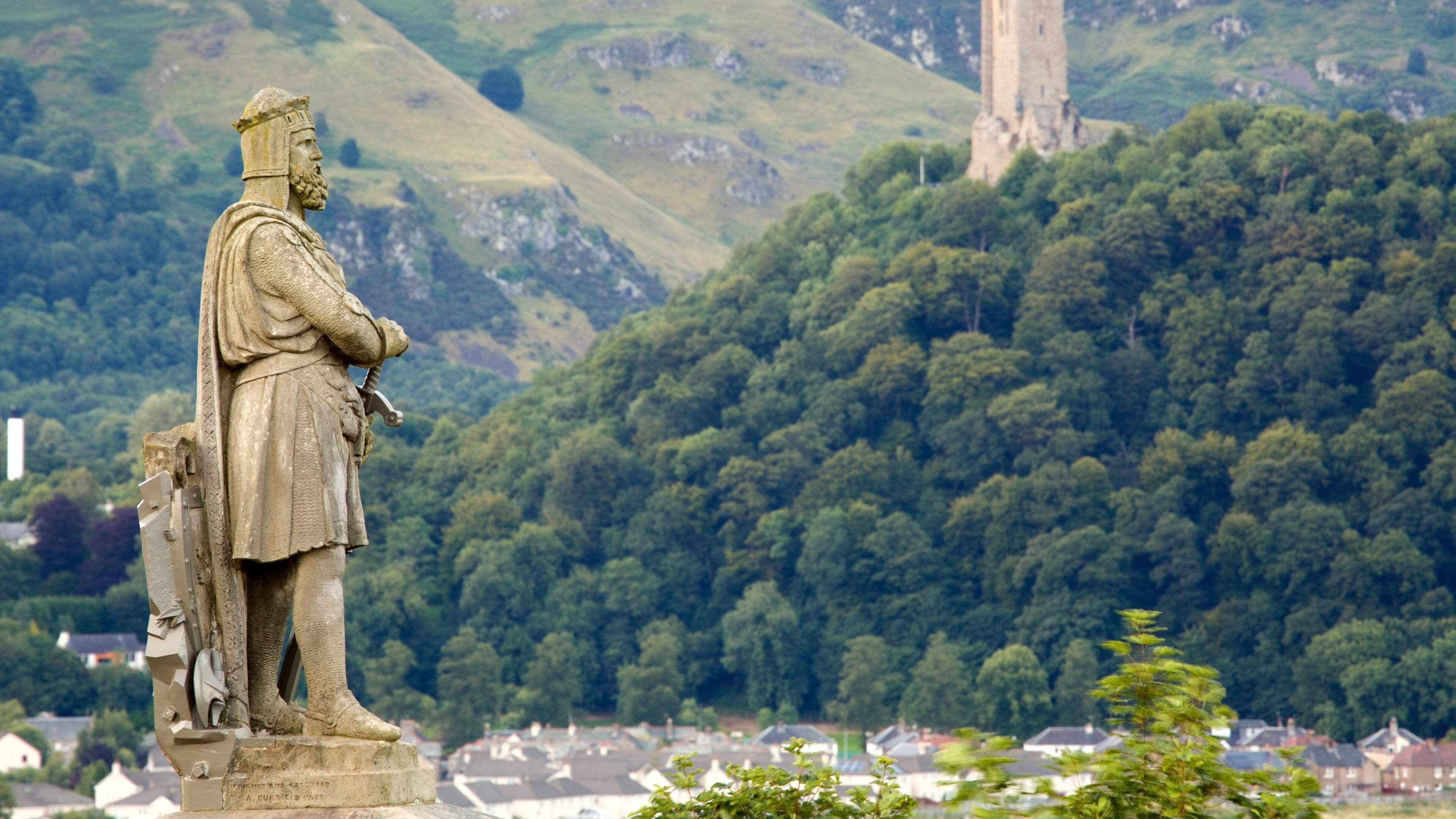 A statue of a historical figure overlooking a densely forested hill with a tower in the background.