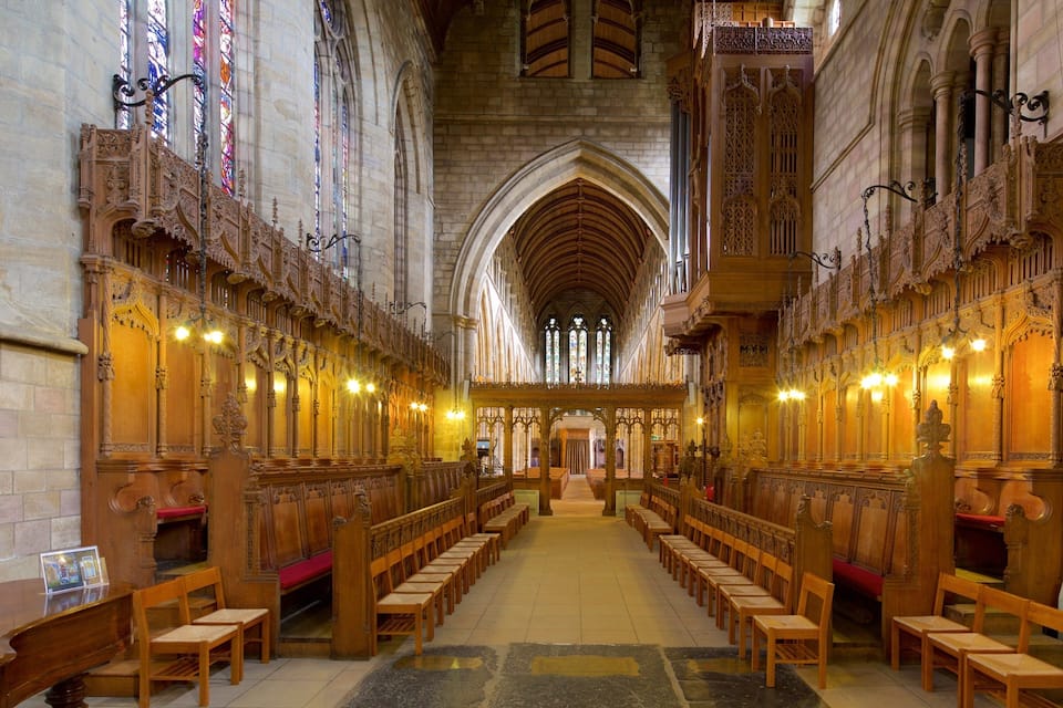 A cathedral interior with wooden pews, stained glass windows, and ornate stone arches.