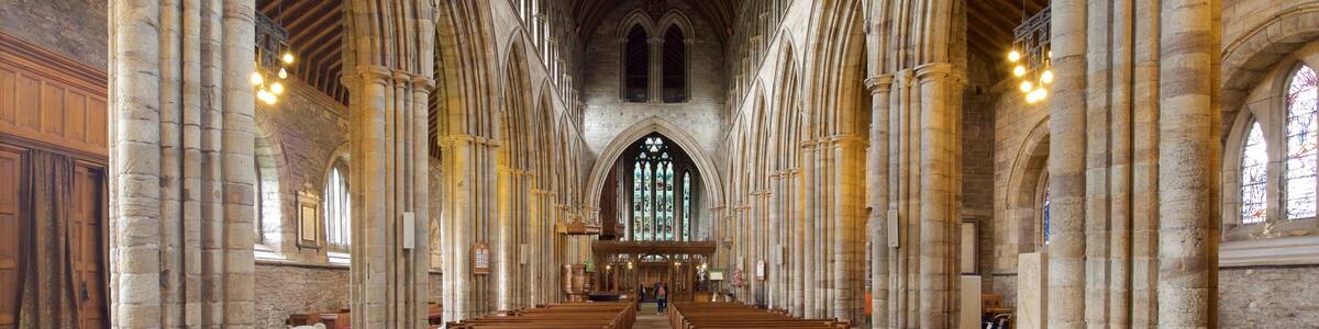 L’intérieur d’une cathédrale, avec de hauts plafonds voûtés, des fenêtres en arc de cercle et des rangées de bancs en bois.