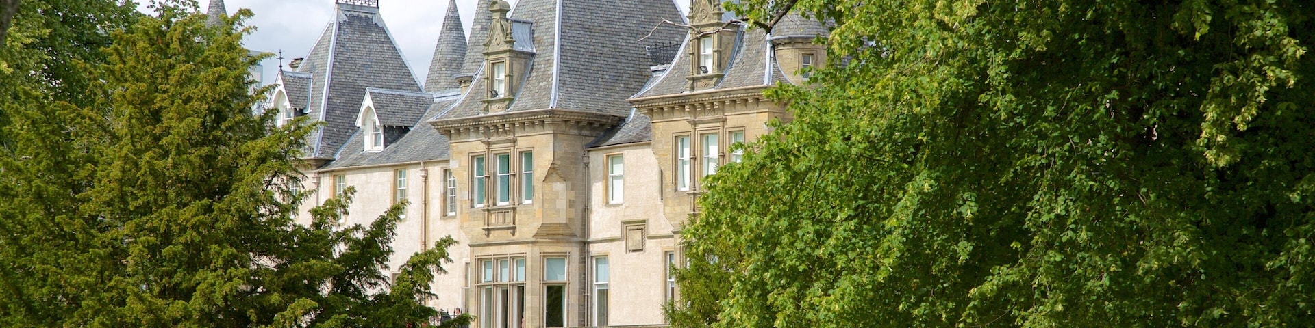 A historic building with multiple towers and a well-maintained lawn.