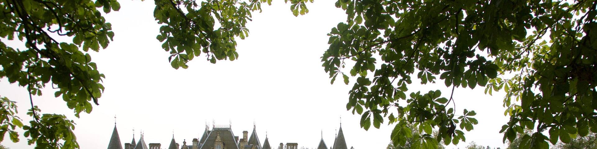 A large, historic building with multiple towers and a well-maintained lawn in front.