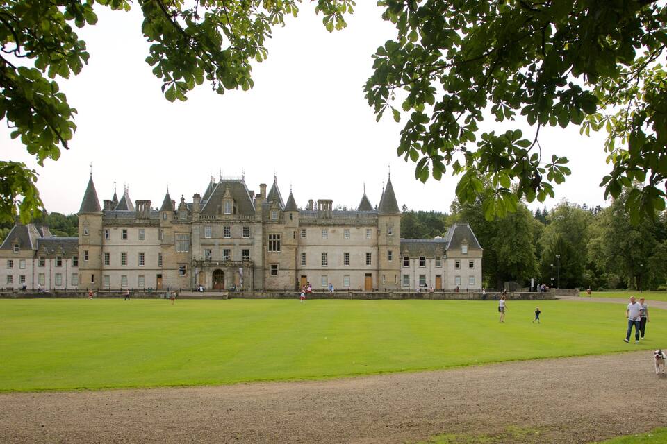 A large, historic building with multiple towers and a well-maintained lawn in front.